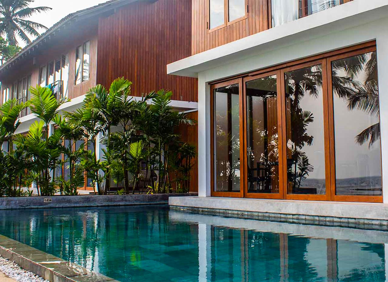 A pool running along the timber-clad side of a villa, with tall glass doors and tropical planting