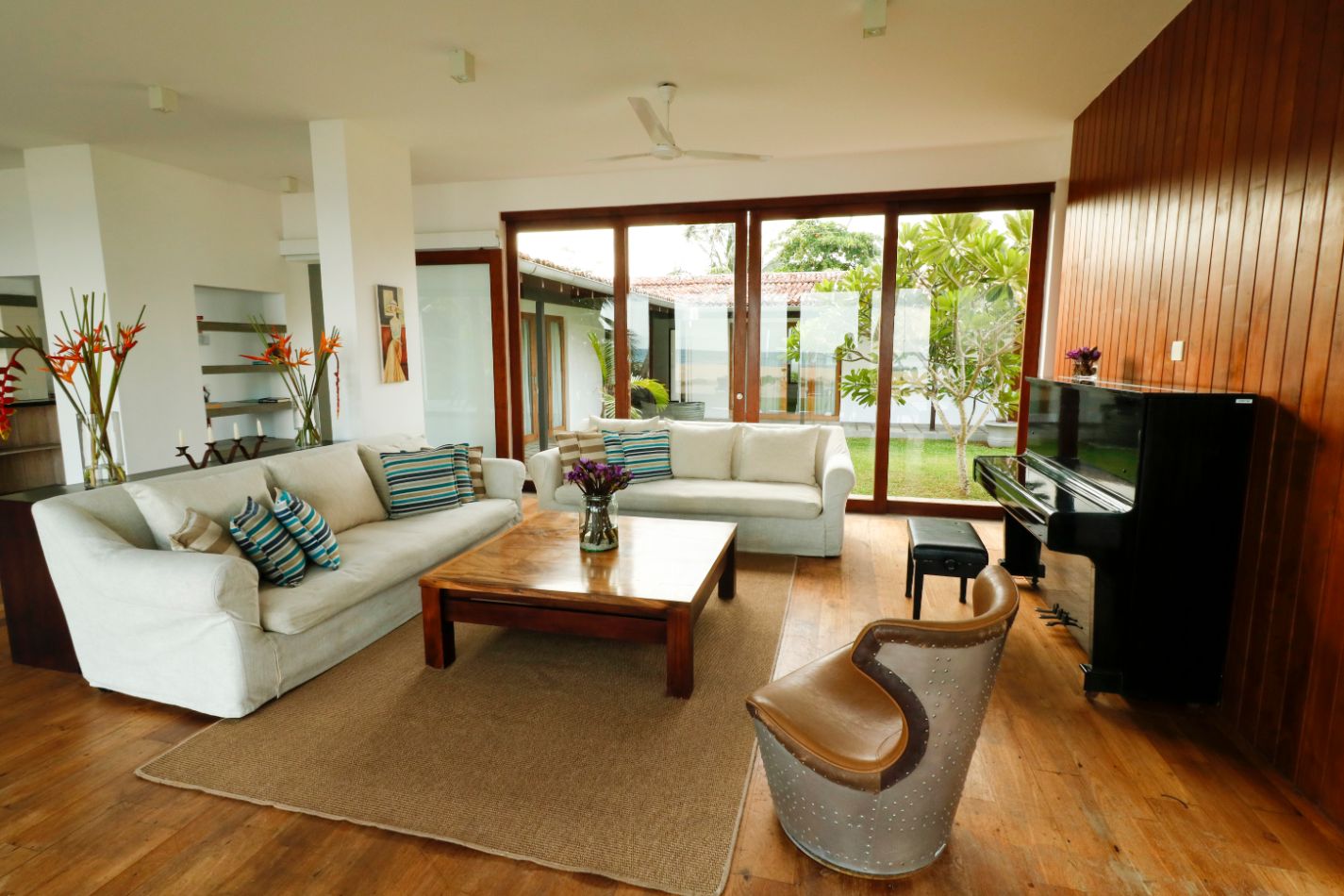 The living room with white sofas, a timber floor, an upright piano and glass doors to the garden