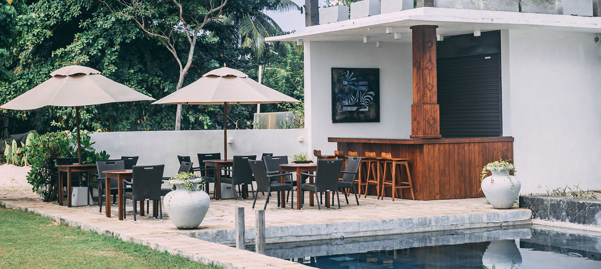 A white bar pavilion with a timber counter and stools, and tables under cream umbrellas beside the pool