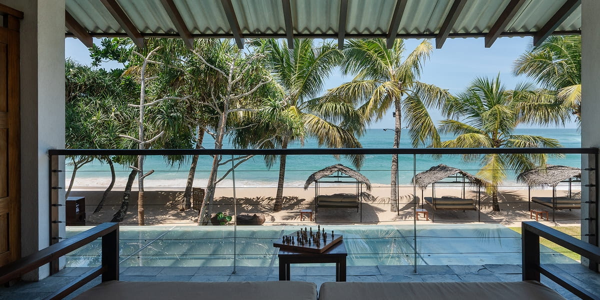 The view from a covered balcony over coconut palms, beach cabanas and the pale blue sea
